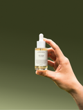 Hand holding a skincare dropper bottle with a gradient green background
